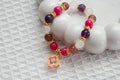 Beaded bracelet with pink, purple, and gold accents on a textured white surface
