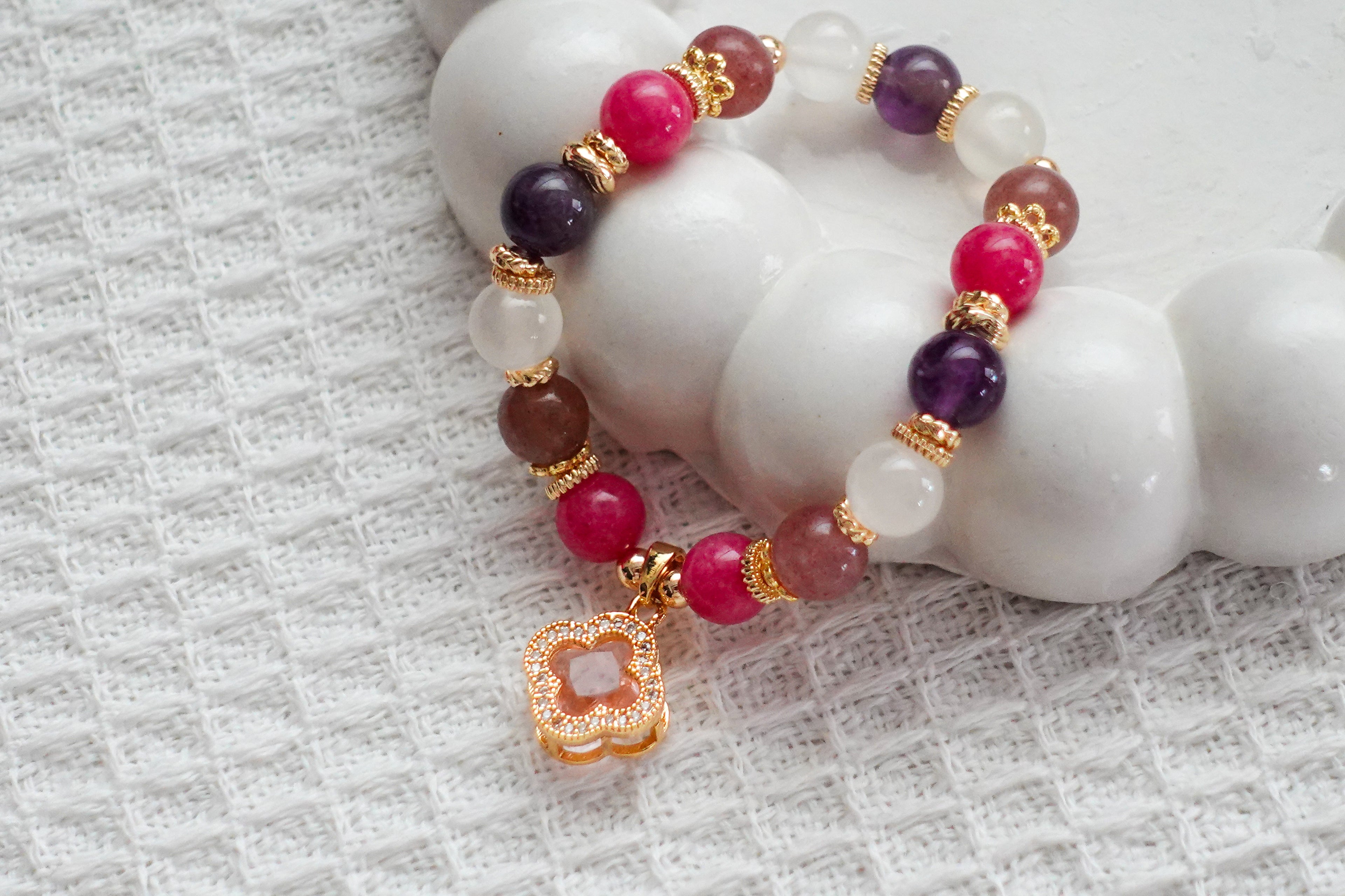 Beaded bracelet with pink, purple, and gold accents on a textured white surface