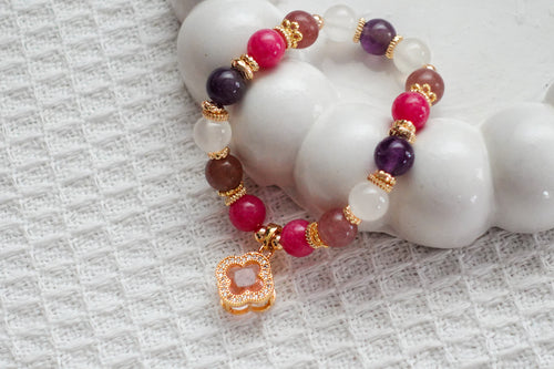 Beaded bracelet with pink, purple, and gold accents on a textured white surface