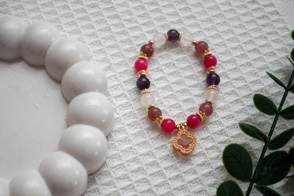 Beaded bracelet with red, purple, and gold accents on a textured surface with white beads.