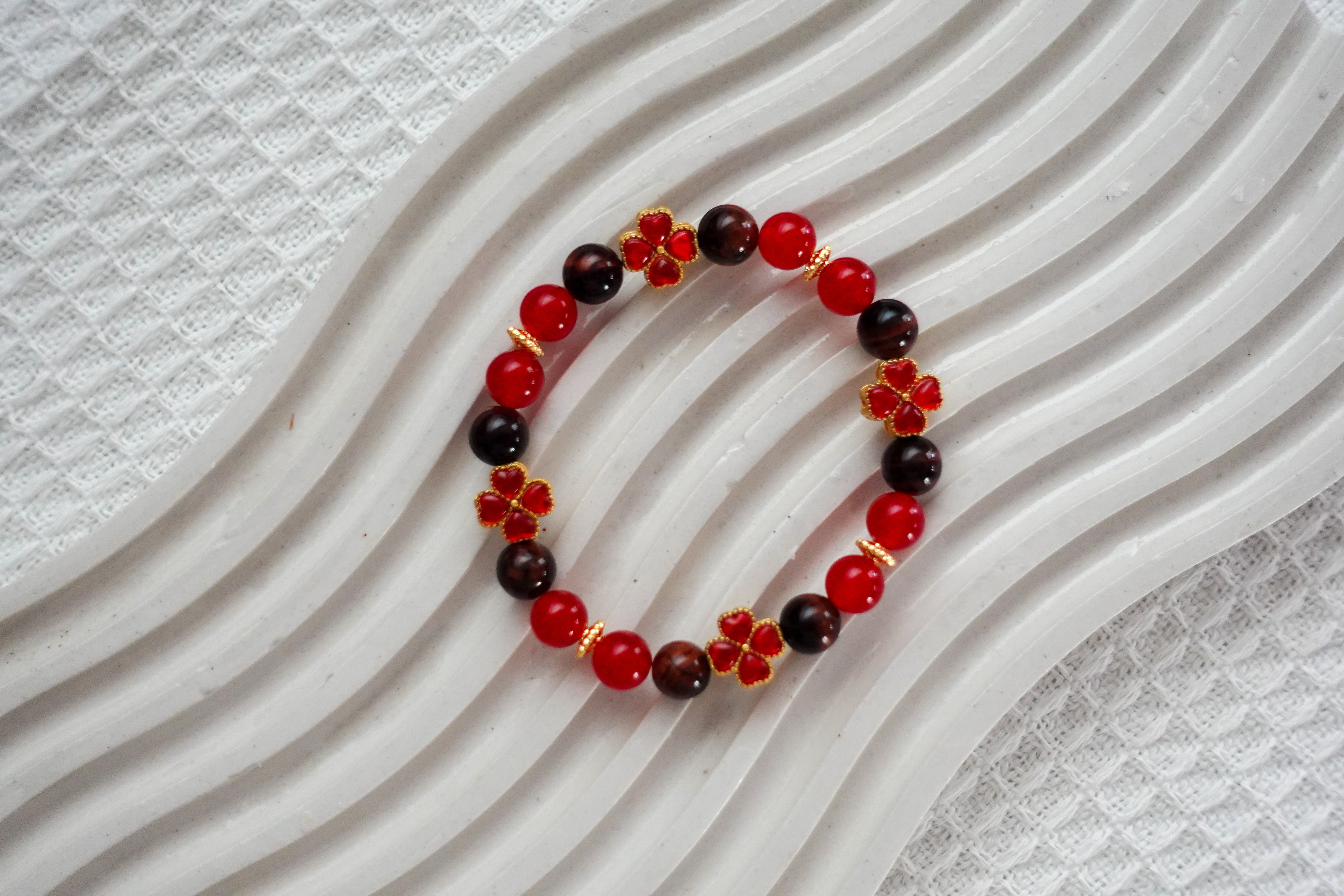 Beaded bracelet with red crystal beads and red 4 four-leaf clover charms on a textured white background