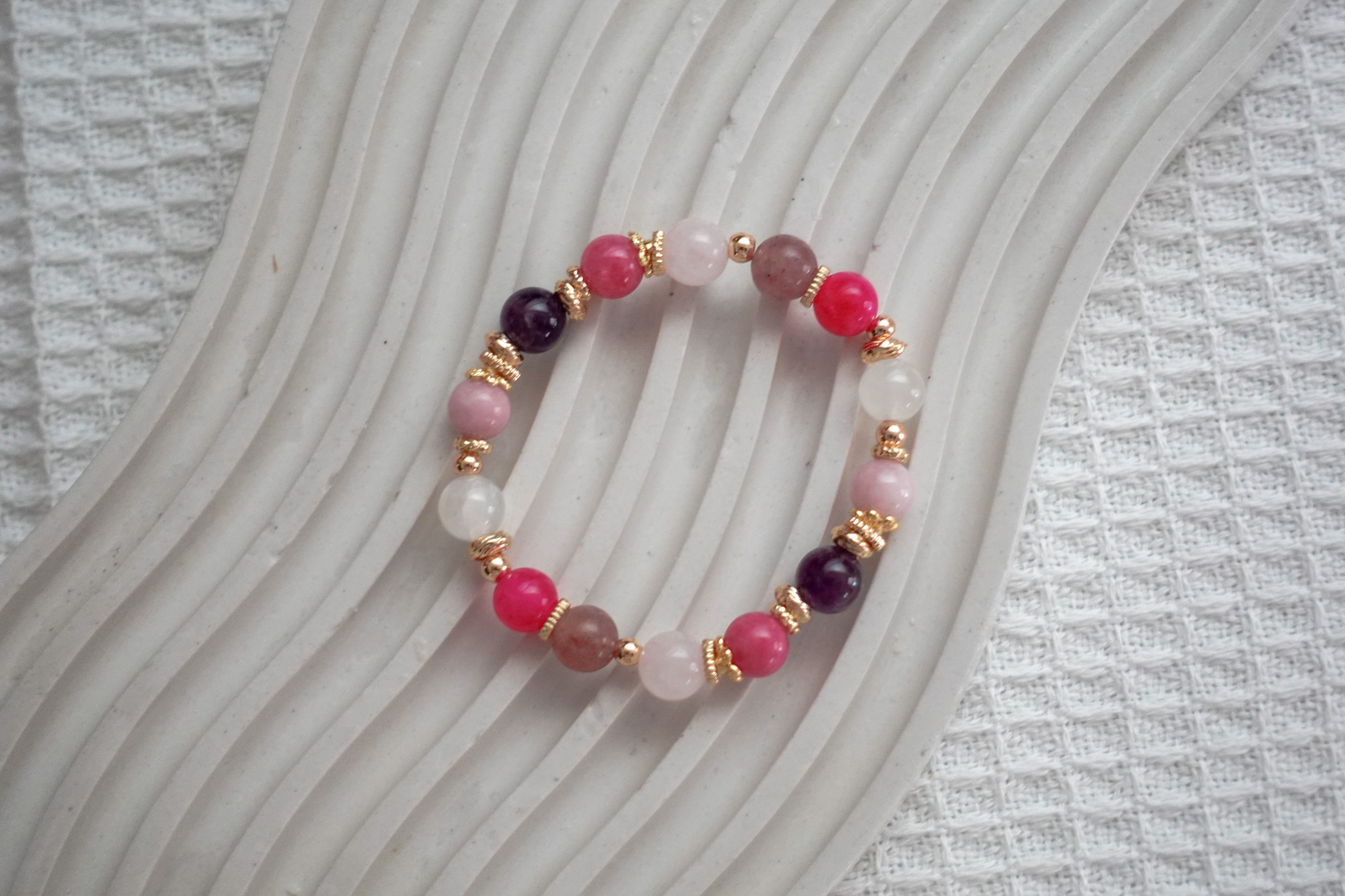Crystal beaded bracelet with pink, purple, and gold accents on a textured surface