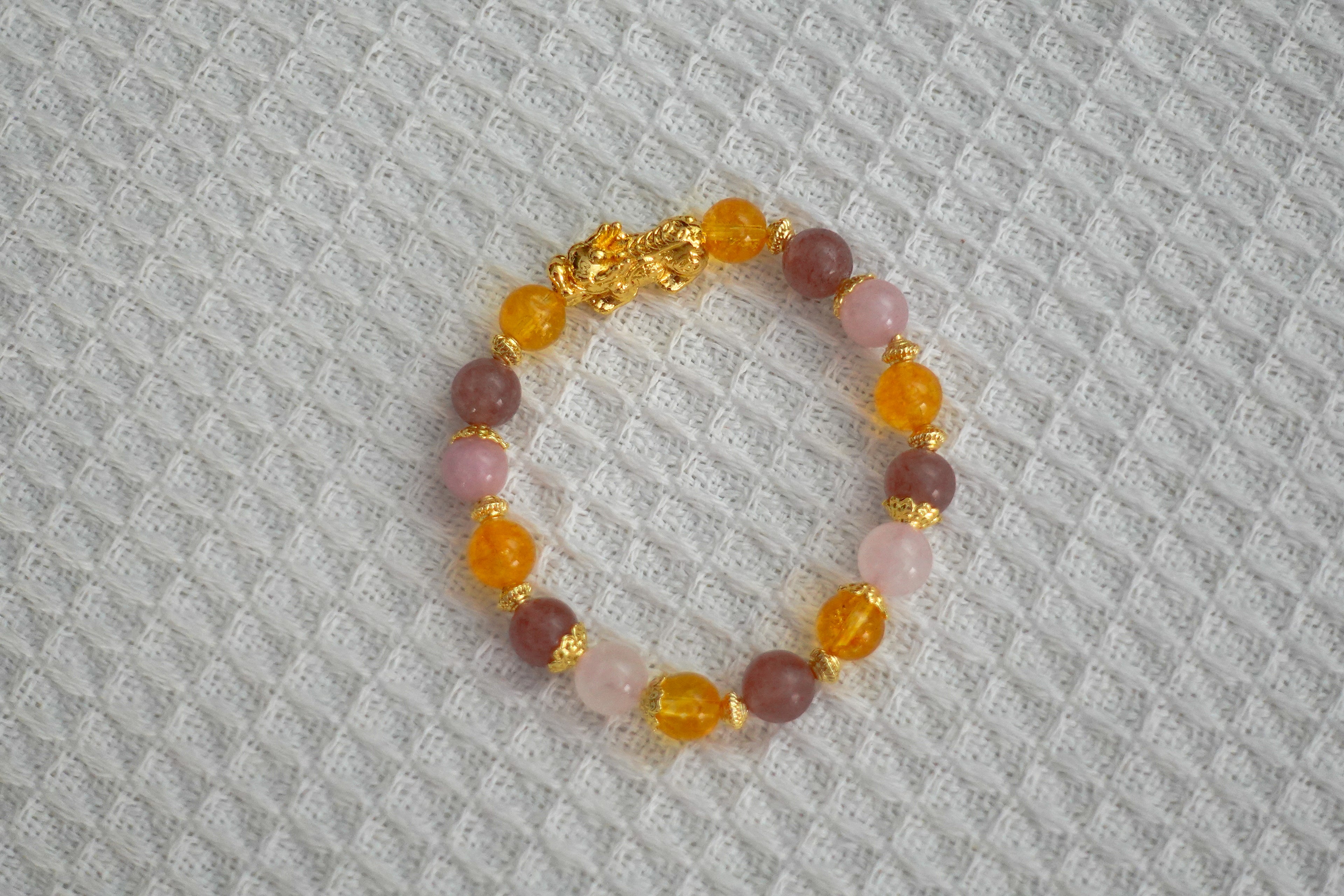 Beaded crystal bracelet with gold Piyao and accents on a textured fabric background