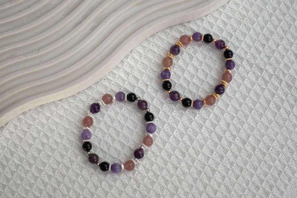 Two purple crystal bracelets with silver and gold hardware on a textured surface