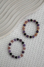 Two purple crystal bracelets with silver and gold hardware on a textured surface